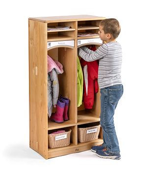 A boy is hanging his jacket into solid maple wood preschool cubbies with baskets