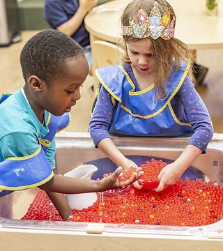 Two children with aprons playing at a sand and water table