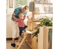 Toddler climbing up the steps of a changing table with the assistance of a teacher